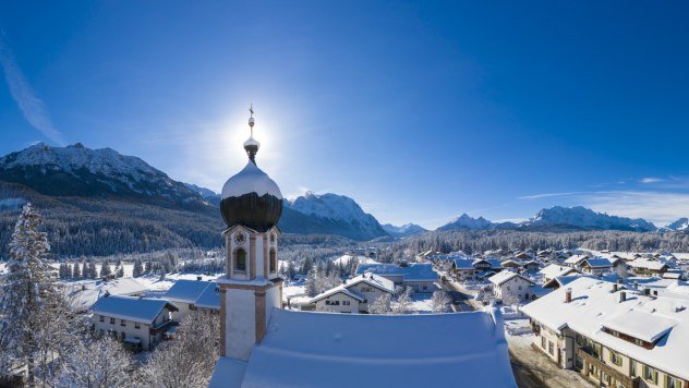 Winter in Krün - church tower with mountain panorama from Seinskopf to Waxensteine., © Alpenwelt Karwendel | Kriner & Weiermann