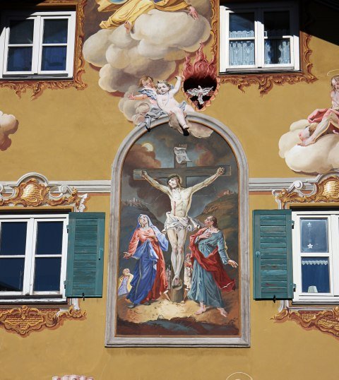 Lüftlmalerei auf einem Haus in Mittenwald mit Jesus am Kreuz in einer Passionsdarstellung. , © Alpenwelt Karwendel | Rudolf Pohmann